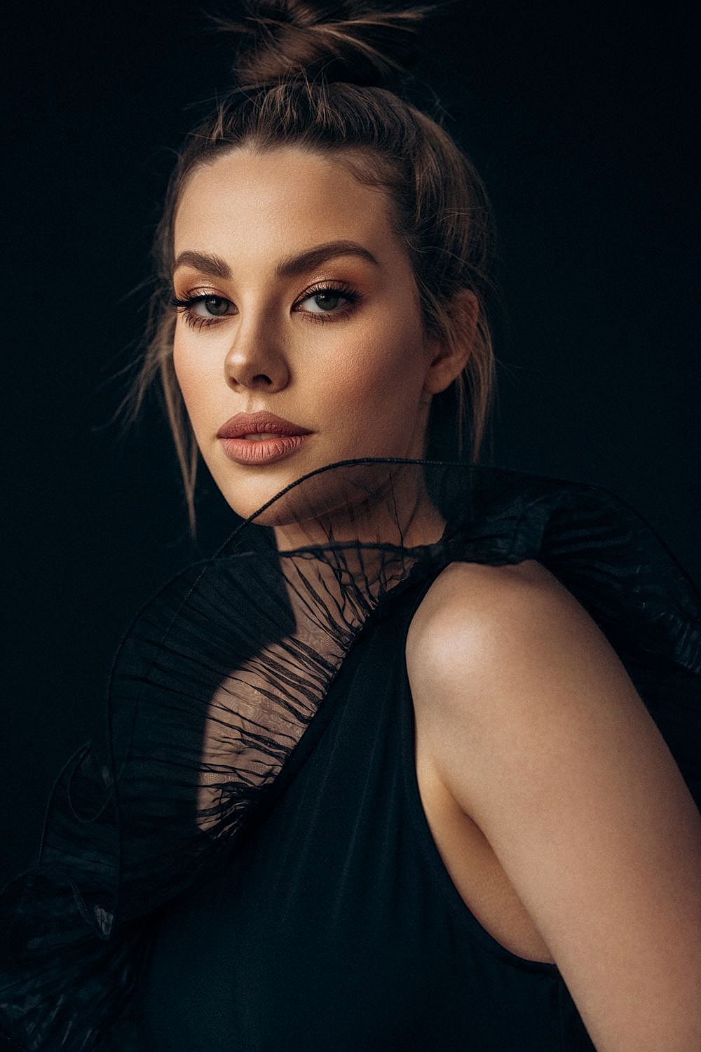 Woman in elegant black fashion against dark background.